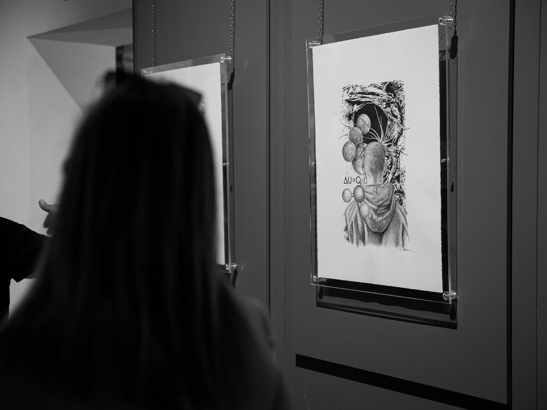 La sagoma scura di una visitatrice in primo piano davanti a un disegno incorniciato e illuminato.
