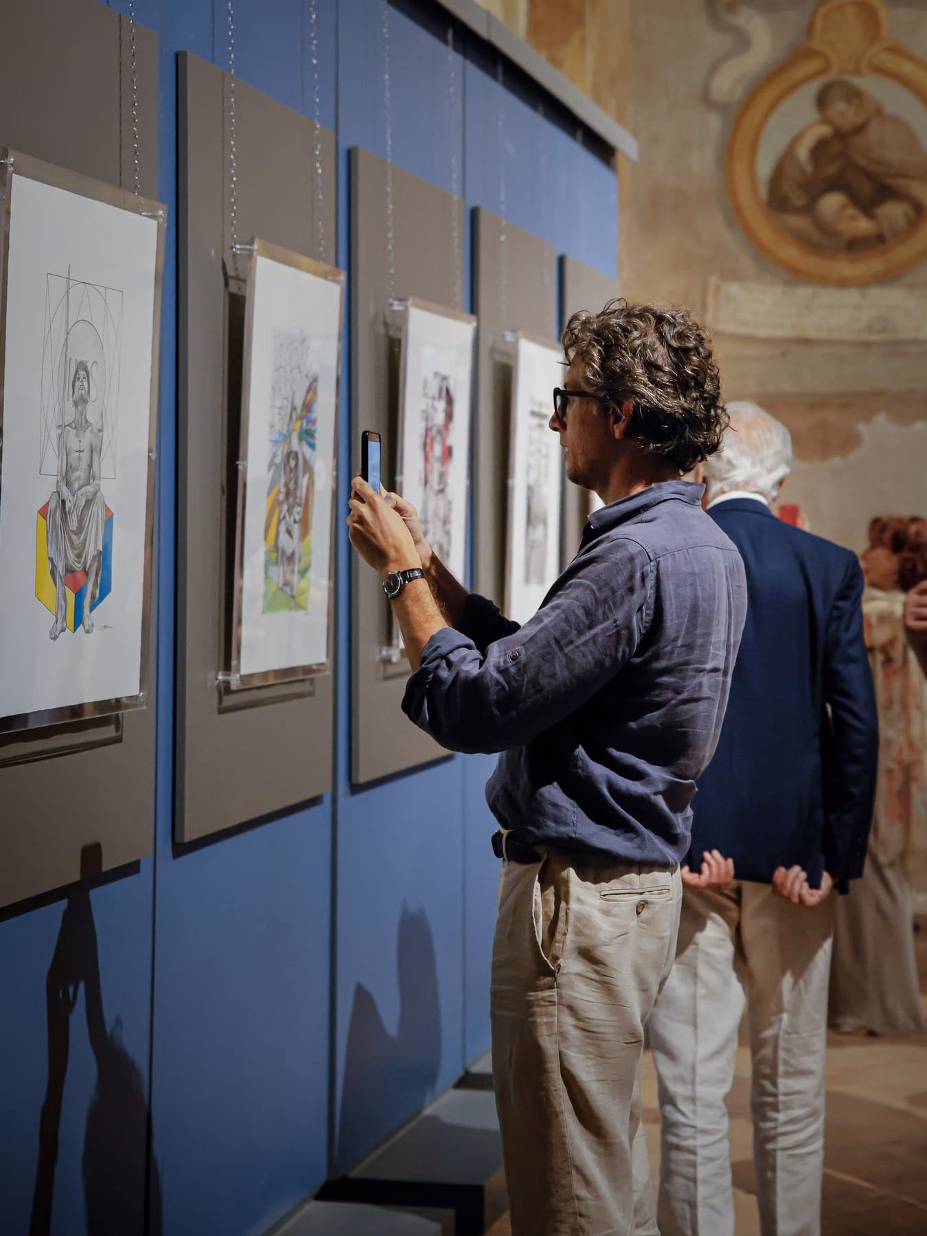 Due visitatori davanti alla parete espositiva: uno indica un disegno all’altro.