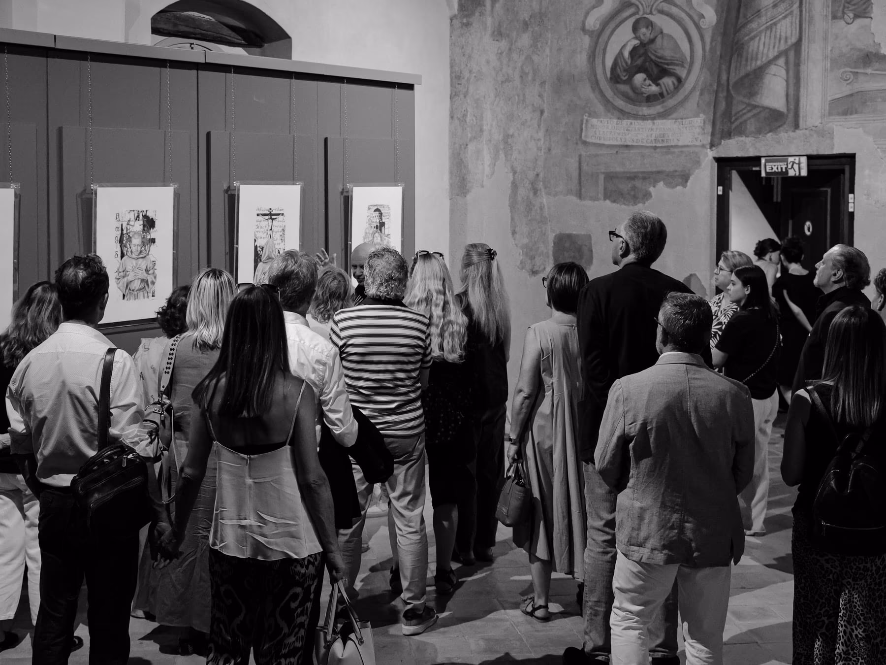 Una folla di visitatori ripresa di spalle mentre osserva la parete delle opere.