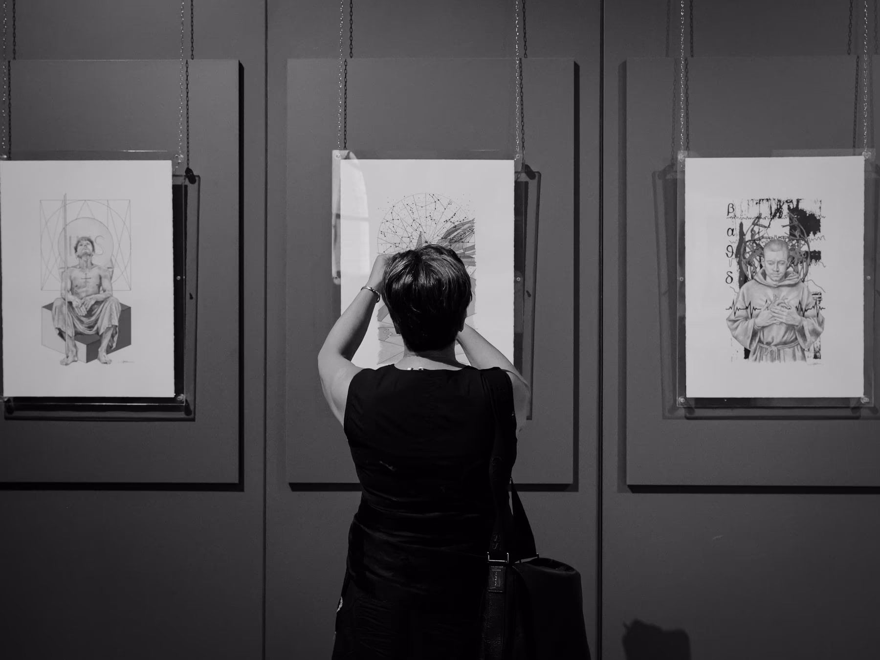 Una visitatrice si sporge fra due pannelli per osservare da vicino un disegno.