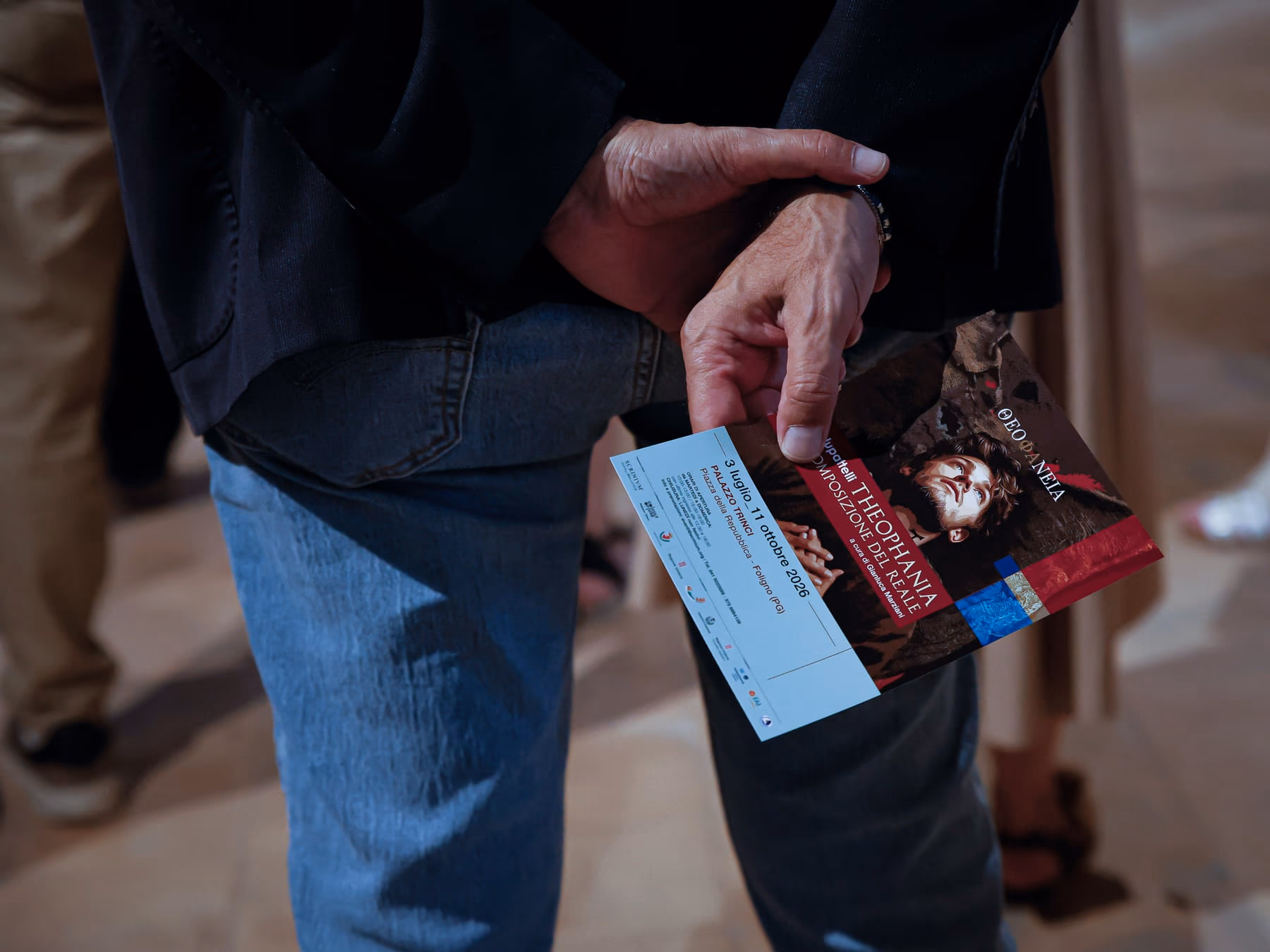 Le mani di un visitatore che tiene il pieghevole della mostra, con il biglietto d’ingresso.