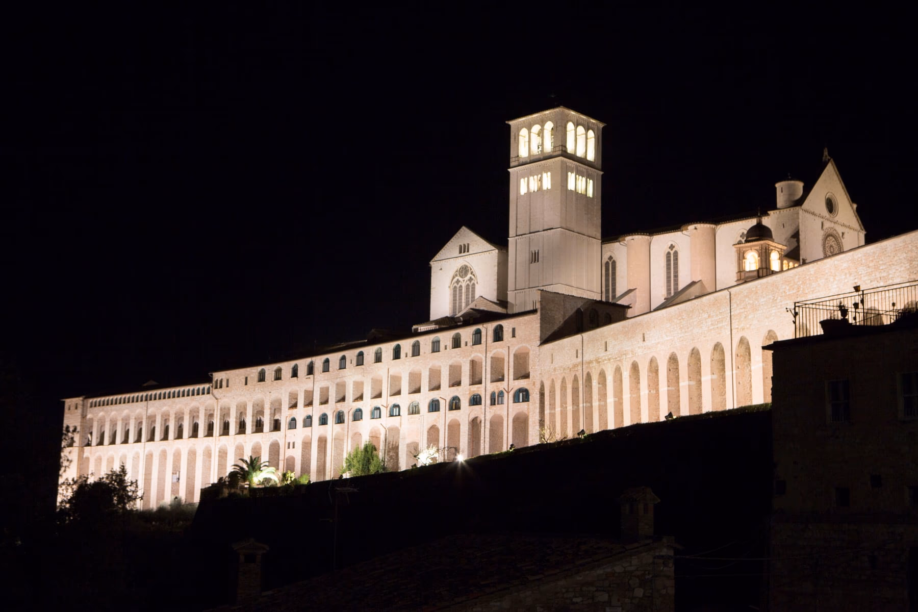 The complex of the Basilica of San Francesco and the Sacred Convent of Assisi lit at night, seen from below.