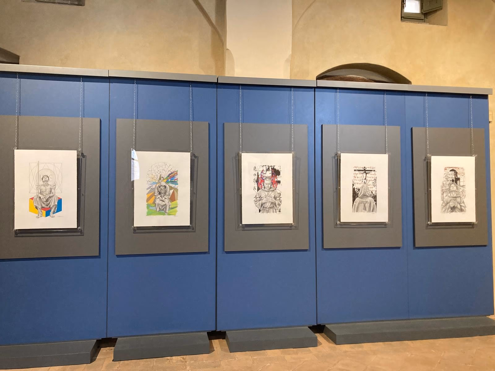 Le tavole di THEOPHANIA incorniciate sui pannelli blu dell’allestimento, in una sala di Palazzo Trinci.