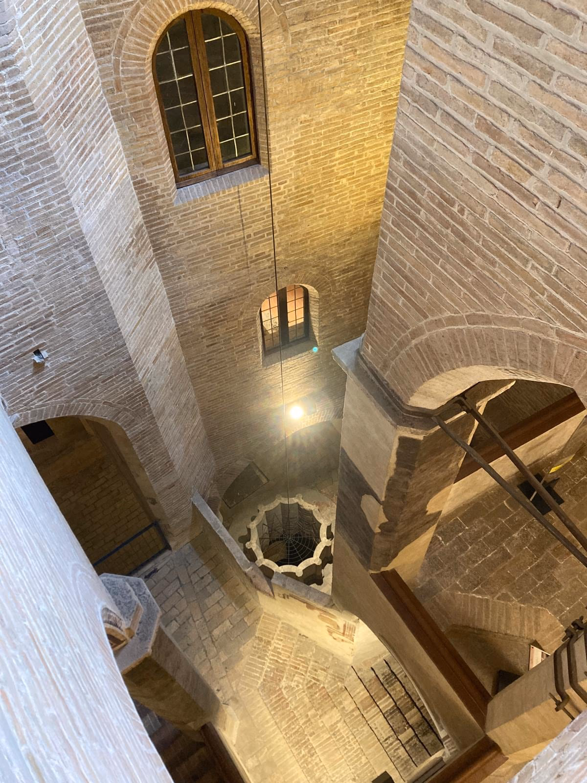 Le volte e la scala interna di Palazzo Trinci viste dall’alto, fra i muri in mattoni e una finestra a inferriata.