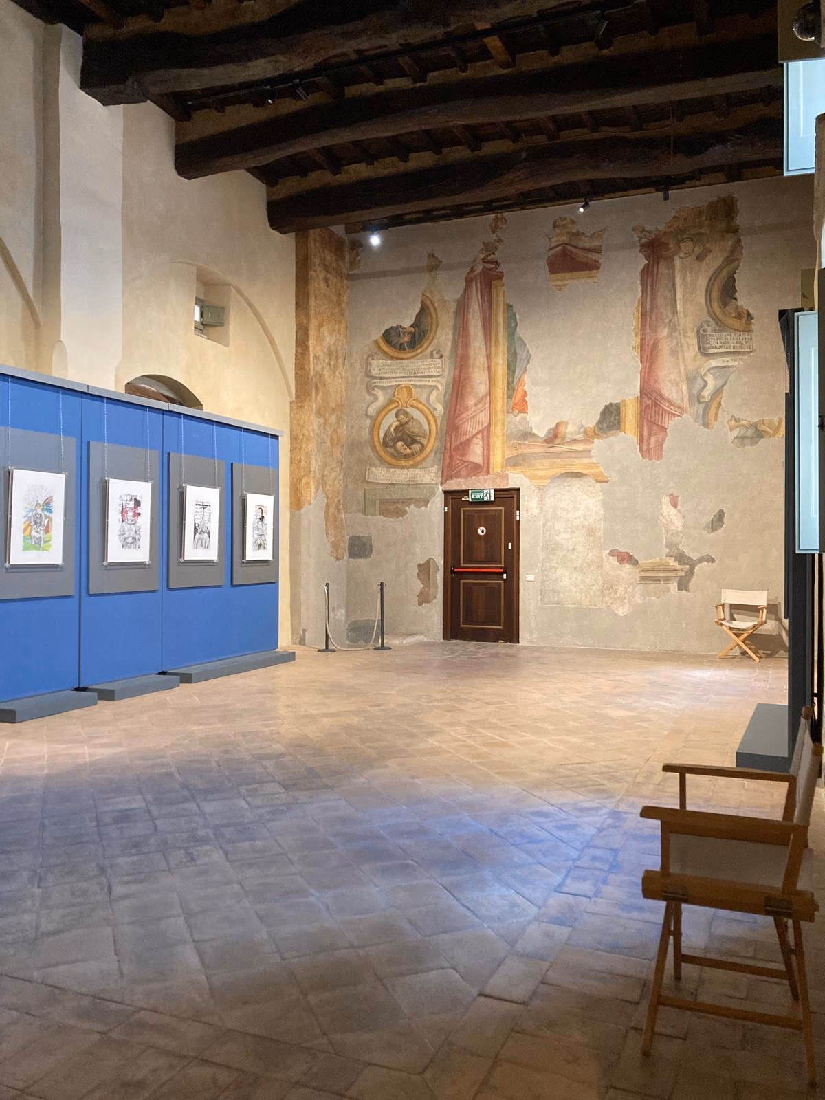 Sala affrescata di Palazzo Trinci con i pannelli dell’allestimento e le opere esposte.