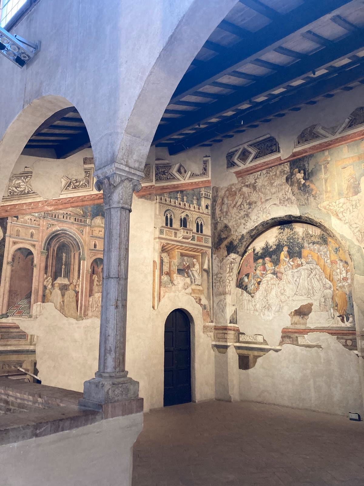 Sala affrescata di Palazzo Trinci con soffitto ligneo e pareti dipinte.